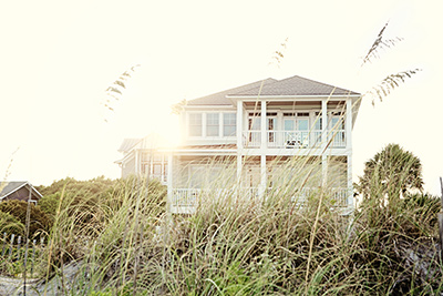 Home builder in Ocean County shows off multi-story coastal home behind beach grass with sun setting behind it 